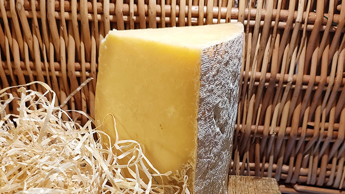 A large wedge of hard cheese in front of a wicker hamper surrounded by hay