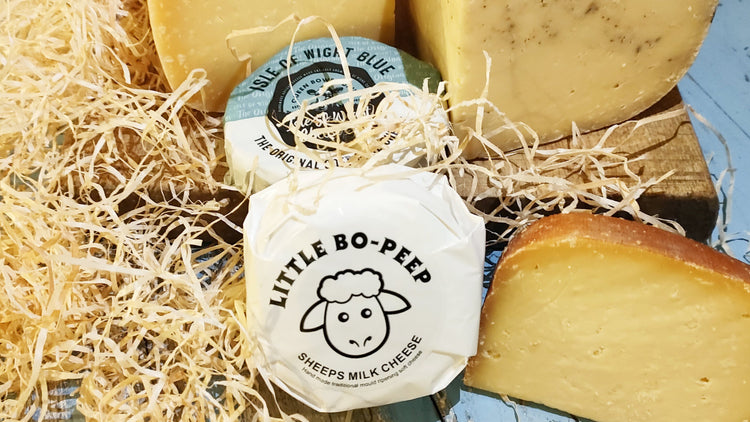 Different cheeses on a chopping board surrounded by hay