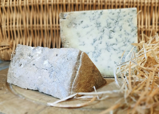 Veiny blue cheese sat on wooden cheeseboard with a hamper backdrop