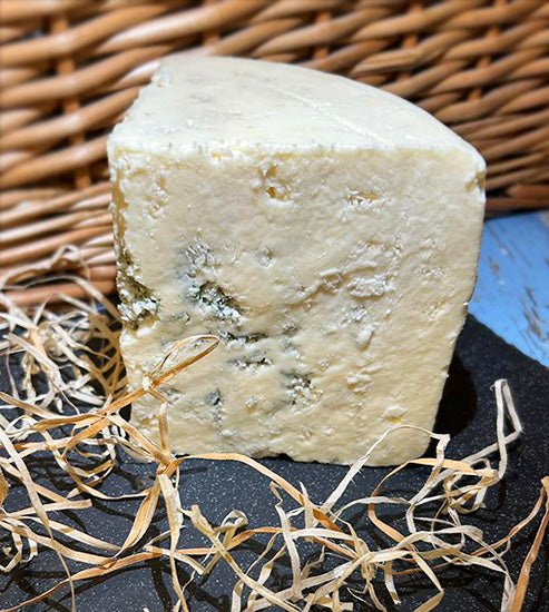 A quarter piece of a wheel of Beenleigh Blue cheese on a slate with a wicker background, surrounded by straw