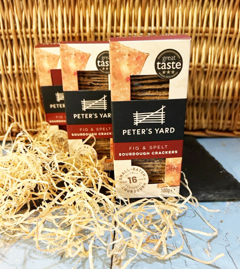 Boxes of fig and spelt crackers in front of a wicker box on slate