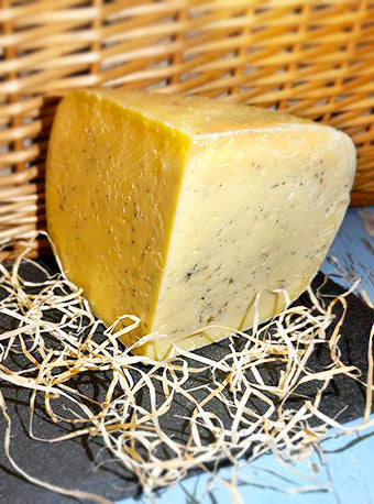 A quarter piece of a wheel of Garlic and Nettle cheese on slate with a wicker background, surrounded by straw