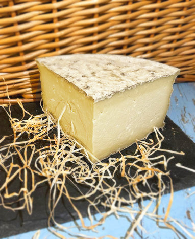 A quarter of a wheel of Gorwydd Caerphilly cheese on a piece of slate with a wicker background, surrounded by straw