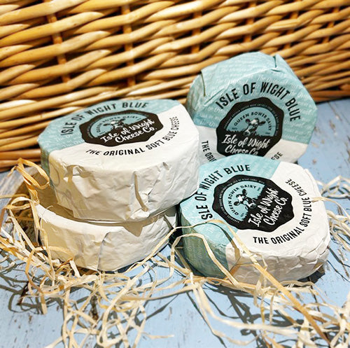 Two piles of Isle of Wight Blue cheese wrapped in blue and white packaging with a wicker background, surrounded by straw