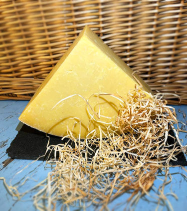 A quarter of a wheel of Montgomery cheddar cheese on a piece of slate with a wicker background, surrounded by straw