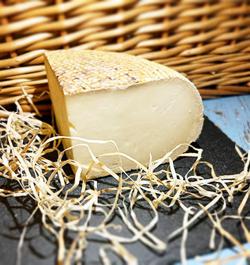 A quarter of a wheel of Rachel cheese on a piece of slate with a wicker background, surrounded by straw