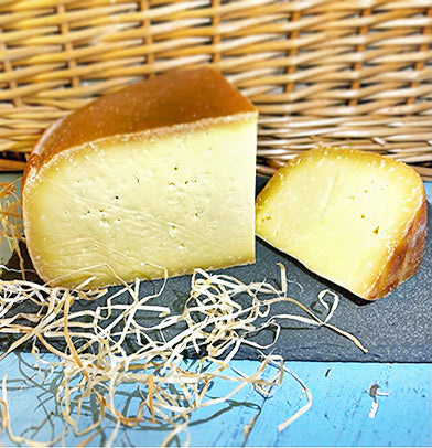 One large and one small piece of Smoked Winchester cheese on slate with a wicker background, surrounded by straw