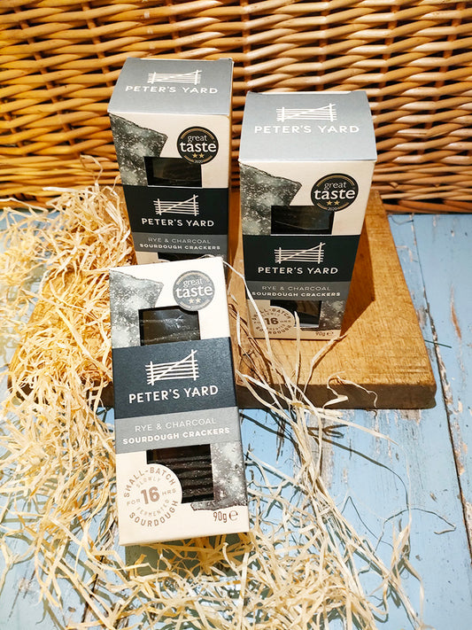 Three boxes of sourdough crackers on a wooden block with a wicker backdrop surrounded by straw