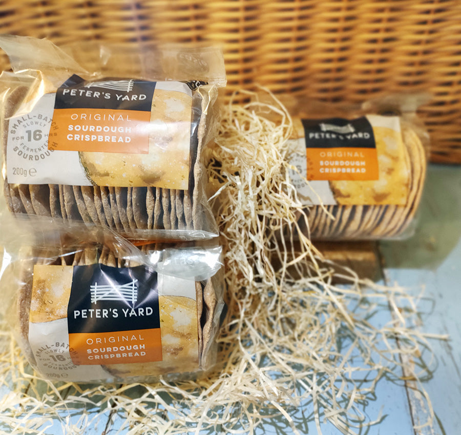 Three packs of sourdough crispbread crackers against a wicker background surrounded by straw